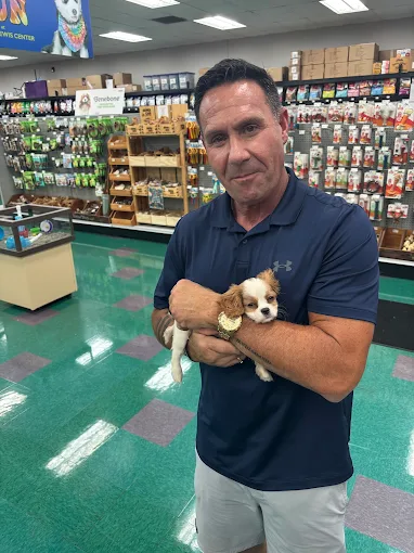 A man holding a small brown and white puppy inside a pet store
